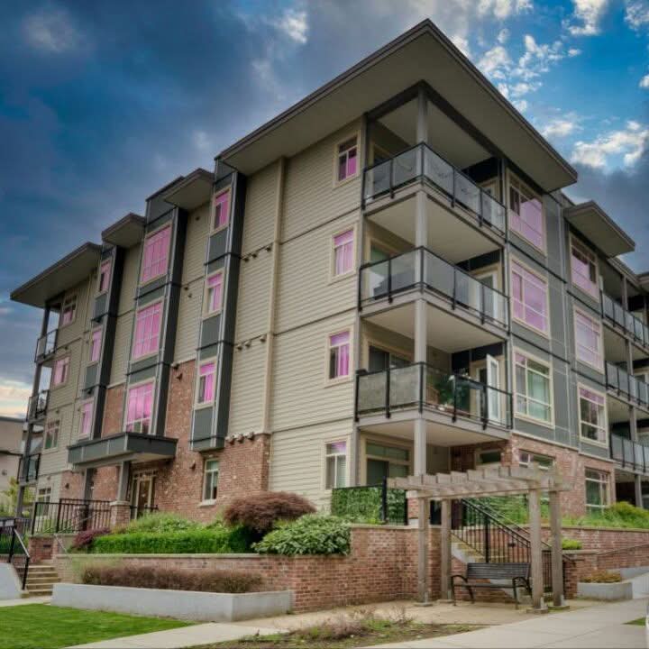 Multi storey residential building with balconies, landscaped frontage and a blue cloudy sky.