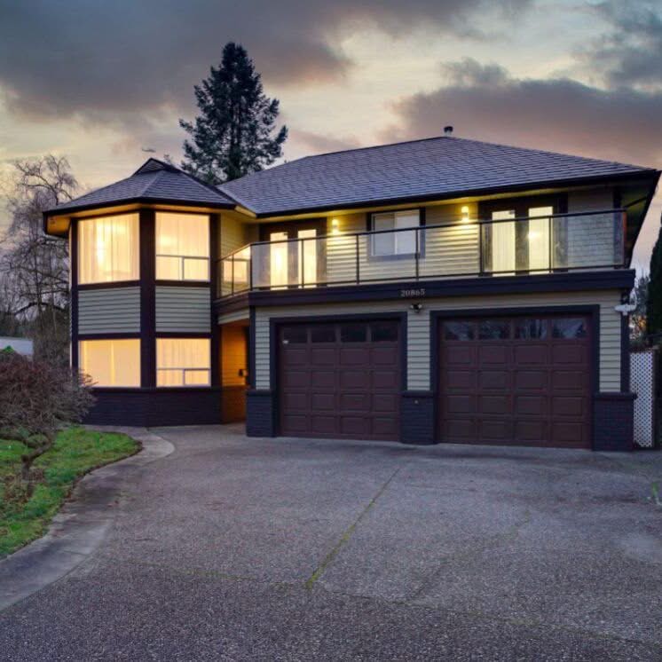 Two storey house with a double garage, illuminated windows and a wide driveway photographed at twilight.