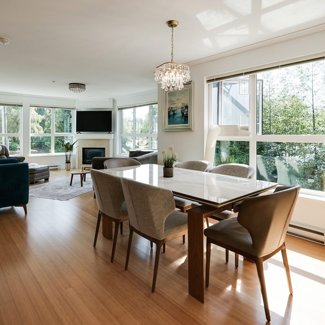 Bright open concept dining room with a wooden table, large windows and an adjoining living area.