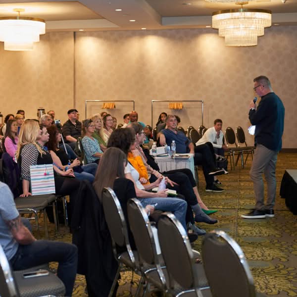 Male speaker presenting to a seated audience inside a conference room