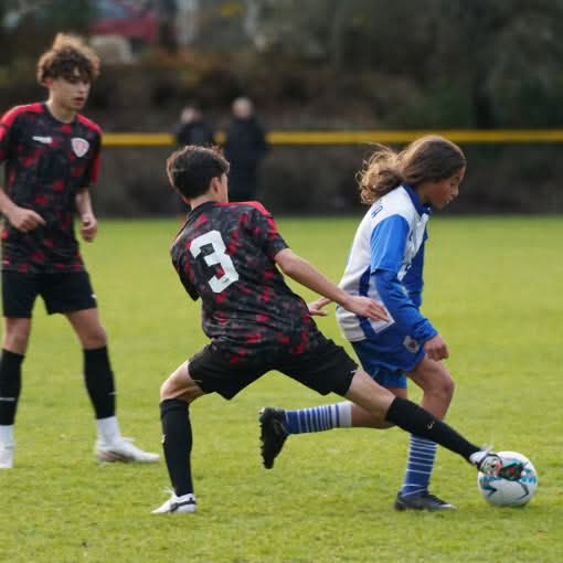 Two young soccer players running and competing for the ball on an outdoor field.