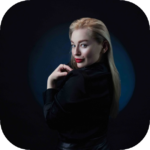 Woman dressed in black posing with her hands near her head against a dark studio background.