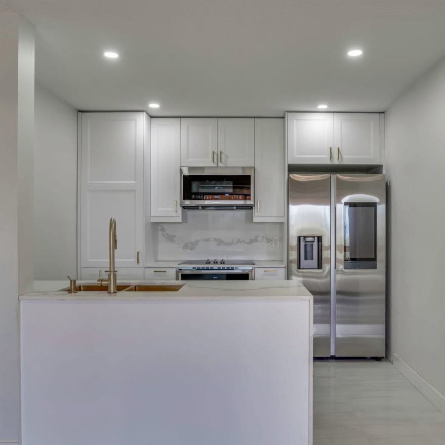 Modern white kitchen with a central island, built in cabinets, stainless steel appliances and recessed lights.