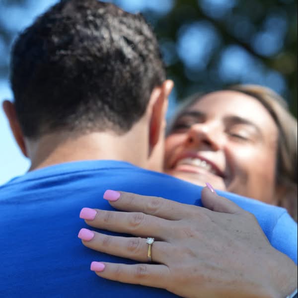 Smiling woman hugging her partner with her engagement ring visible on his blue shirt