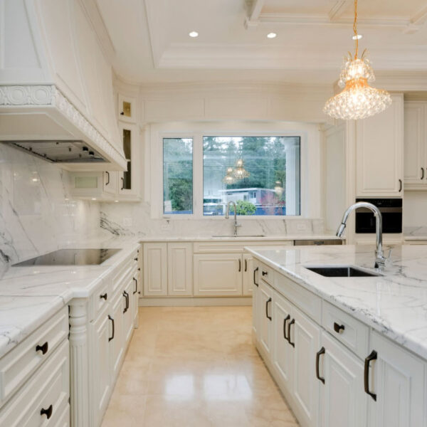 Bright white galley kitchen with cabinets on both sides, light flooring, pendant lighting and a window at the far end.