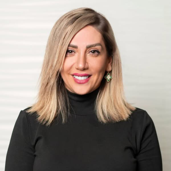 Blonde woman in a black turtleneck facing the camera with a warm smile against a light grey background