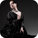 Woman in an elaborate black outfit posing against a dark background during a creative studio production.
