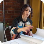 Woman seated at a table demonstrating an item during a business social media video session.