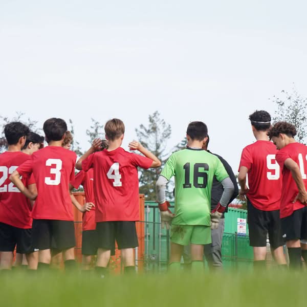 Youth soccer team in red jerseys gathered with a goalkeeper wearing a green number 16 uniform