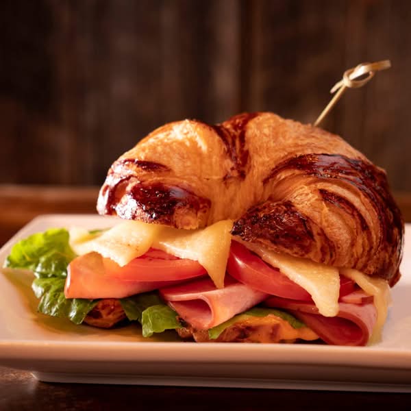 Golden croissant sandwich filled with sliced meat, cheese, tomato and lettuce on a plate