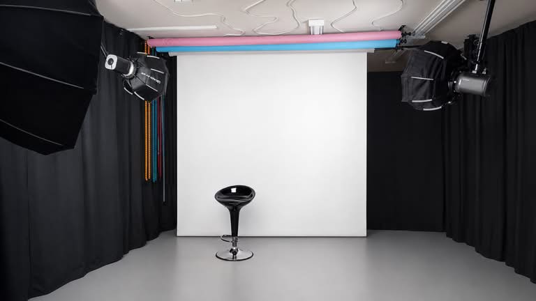 Professional photography studio with a white backdrop, black curtains, lighting equipment and posing stool