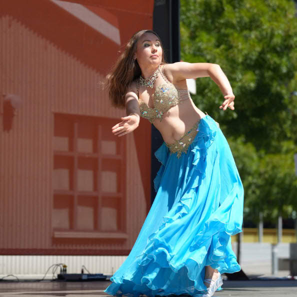 Female dancer performing outdoors in a gold top and flowing blue skirt during a cultural event