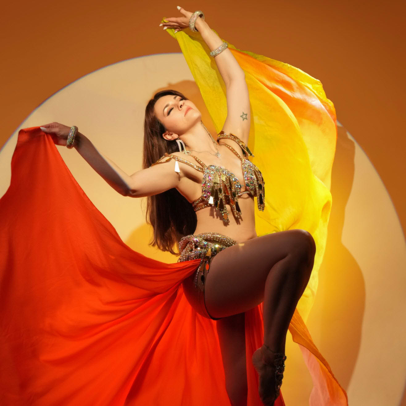 Female dancer performing with flowing orange and yellow fabric against a warm circular studio backdrop