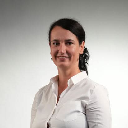 Professional woman wearing a white blouse with her hair tied back, smiling against a bright studio background