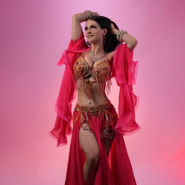 Woman posing in a bright red fashion outfit with flowing fabric against a pink studio background
