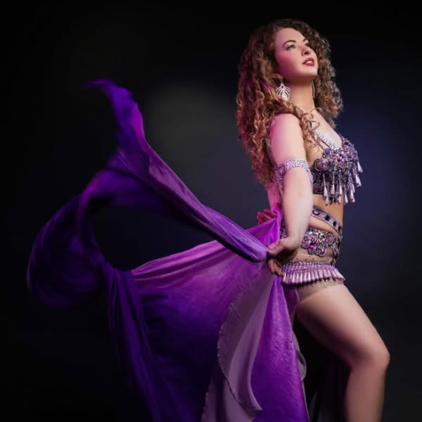 Woman lifting a flowing purple dress during a dramatic glamour photography session against a dark background