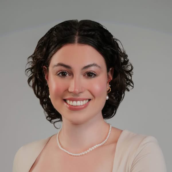 Smiling woman with short curly dark hair wearing a light top and pearl necklace in a professional studio headshot