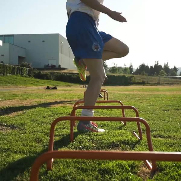 thlete stepping over red agility hurdles during an outdoor soccer training session