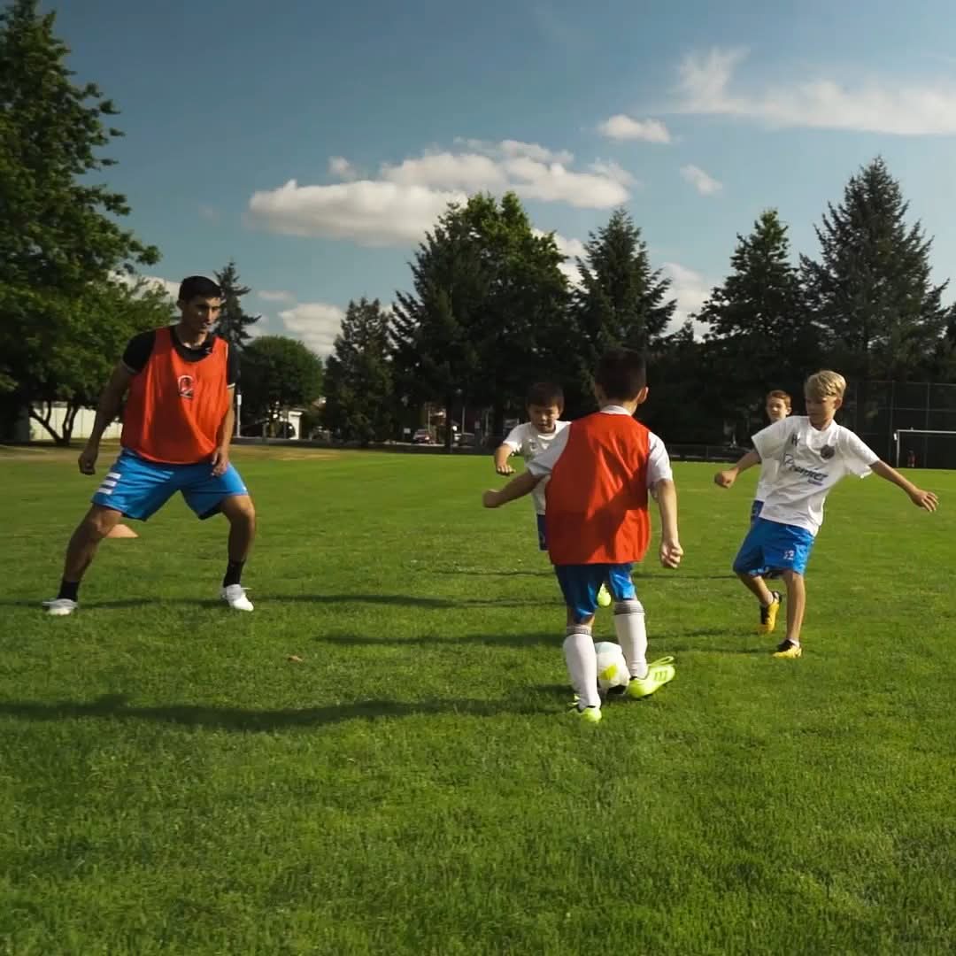 Youth soccer players in orange and white training jerseys competing for the ball on a grass field
