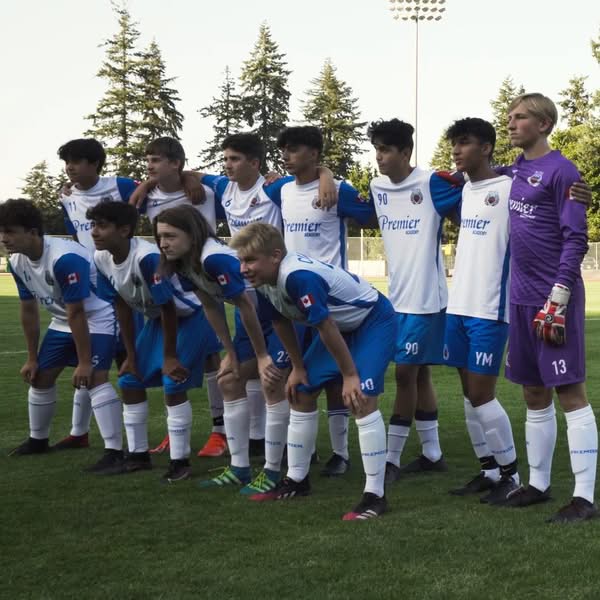 Youth soccer team in blue and white uniforms posing together with coaches on an outdoor field