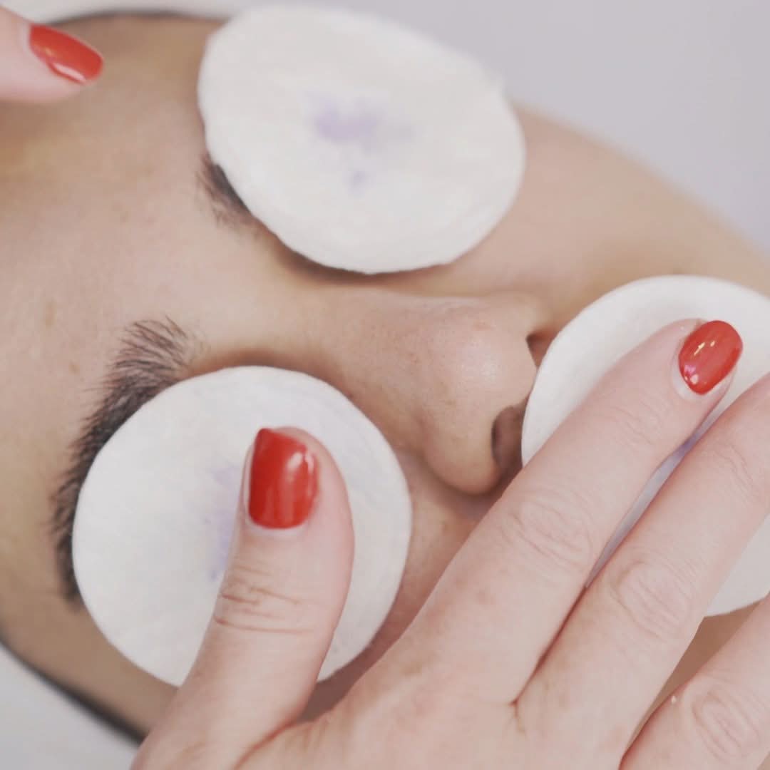 Close view of a woman receiving a facial treatment with cotton pads placed over her eyes and a hand touching her face